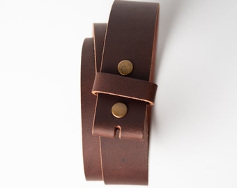 May include: A brown leather belt strap with two brass rivets. The strap is folded in half and the ends are overlapping.