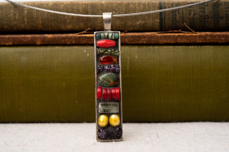 Puede incluir: Un collar de plata con un colgante rectangular hecho de azulejos de mosaico de colores. El colgante presenta azulejos rojos, verdes, azules y amarillos.