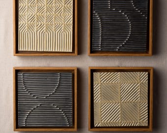 May include: Four square ceramic wall art pieces with different geometric patterns. Each piece is framed in a natural wood frame.