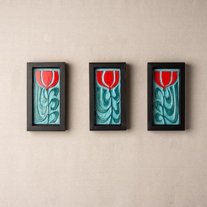 Könnte beinhalten: Drei gerahmte Kunstwerke mit floralem Design. Jedes Stück zeigt eine rote Tulpe vor einem türkisfarbenen Hintergrund, in schwarzen Rahmen. Die Kunstwerke sind an einer neutralen Wand ausgestellt und bilden ein zusammenhängendes Set.