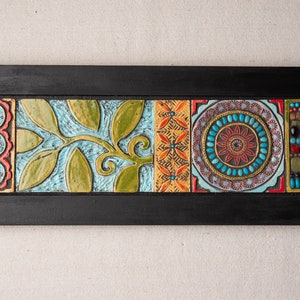 May include: A framed wall art piece with a mosaic design. The mosaic features a leafy vine, a geometric pattern, a circular design with turquoise and red accents, and a vertical row of colorful beads.