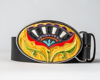 May include: Oval belt buckle with a colourful floral design. The buckle features a yellow background with a red, blue, and green flower design. The buckle is set on a black leather belt.