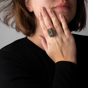 May include: A silver ring with a colorful rectangular stone. The stone has a mosaic design with red, green, blue, and yellow colors.