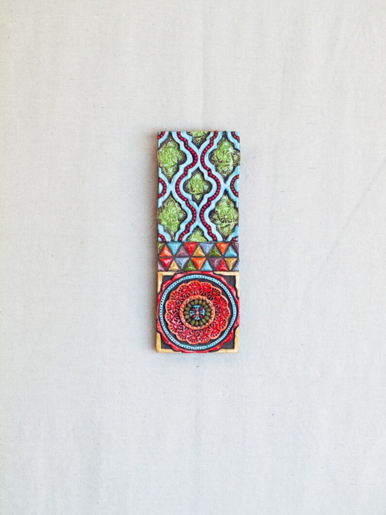 May include: A colorful tile with a geometric pattern in shades of green, blue, red, and yellow. The tile has a circular design in the center with a cross in the middle.