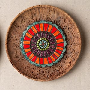 Puede incluir: Un plato redondo de madera con un diseño de mosaico de azulejos coloridos en el centro. El diseño de los azulejos presenta un patrón circular de rojo, naranja, azul, verde y morado.