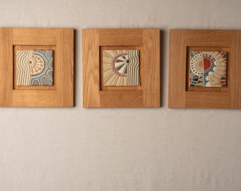 Pode incluir: Três azulejos de cerâmica emoldurados com desenhos geométricos abstratos em tons de azul, vermelho, branco e preto. Os azulejos são emoldurados em madeira natural.