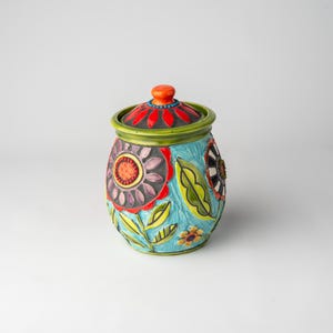 May include: A colorful ceramic jar with a lid, decorated with flowers and leaves in shades of red, orange, yellow, green, blue, and purple.