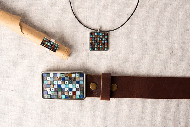 May include: A set of three jewelry pieces featuring a mosaic design with a variety of colorful stones. The set includes a necklace, a ring, and a belt buckle.