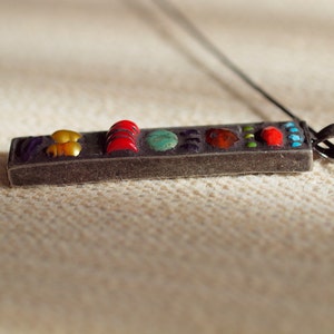 May include: A silver pendant with a rectangular shape and a variety of colorful stones. The stones are arranged in a row and include red, yellow, green, blue, and purple.