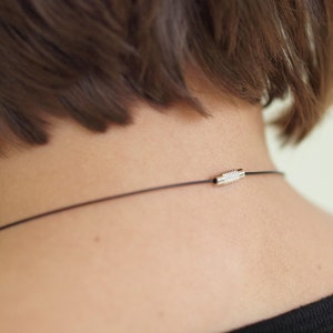 May include: A close-up of a person's neck with a black cord necklace featuring a silver clasp.