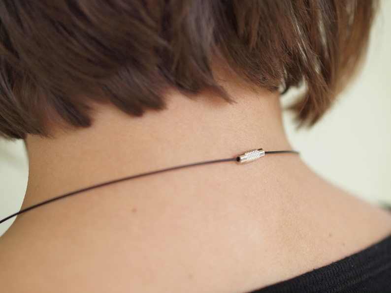 May include: A close-up of a person's neck with a black cord necklace featuring a silver clasp.