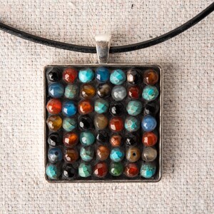 May include: A square pendant necklace with a silver frame and a mosaic of colorful stones. The stones are set in a grid pattern and include shades of blue, green, red, and brown.