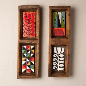 Könnte beinhalten: Zwei Holztabletts mit jeweils drei rechteckigen Keramikfliesen. Die Fliesen zeigen abstrakte geometrische Muster in verschiedenen Farben, darunter Rot, Grün, Blau, Gelb, Schwarz und Weiß.