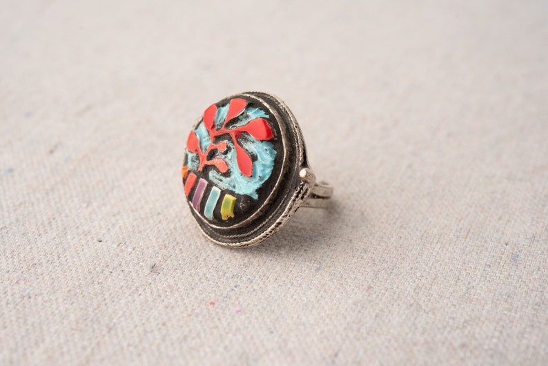 Pode incluir: Um anel de prata com um design redondo de esmalte colorido. O design apresenta um fundo azul com detalhes vermelhos, amarelos e roxos.
