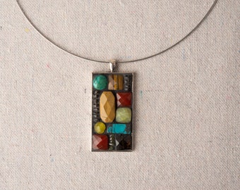 Puede incluir: Un collar de cadena de plata con un colgante rectangular hecho de varias piedras de colores, incluyendo turquesa, rojo, amarillo y marrón.