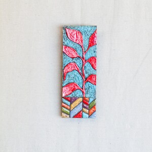 May include: A rectangular wall hanging with a blue background and a red stylized plant design. The bottom of the hanging has a colorful geometric pattern.