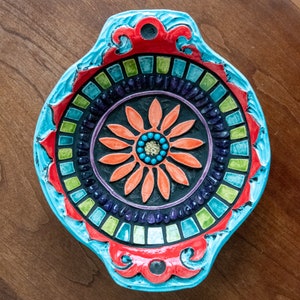 May include: A blue and red ceramic dish with a mosaic design featuring a colourful flower in the centre.