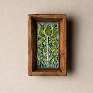 May include: A rectangular wooden tray with a carved floral tile insert. The tile features a green stylized flower design on a teal background. The wooden tray has a natural, warm brown color.