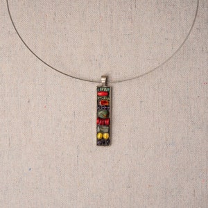 Puede incluir: Un collar de cadena de plata con un colgante rectangular hecho de azulejos de mosaico de colores. El colgante presenta azulejos rojos, amarillos, verdes y azules.