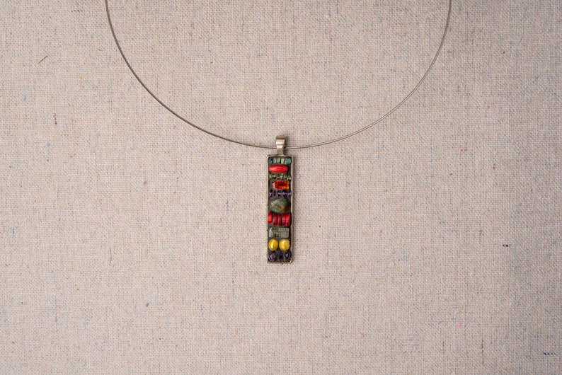 Puede incluir: Un collar de cadena de plata con un colgante rectangular hecho de azulejos de mosaico de colores. El colgante presenta azulejos rojos, amarillos, verdes y azules.