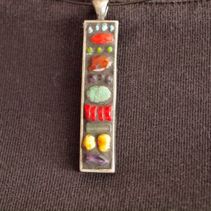 May include: A silver pendant necklace with a rectangular charm featuring a mosaic of colorful stones, including red, orange, yellow, green, blue, and purple.