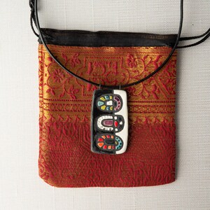 May include: A black cord necklace with a rectangular pendant. The pendant is made of white and black ceramic with colorful geometric designs.