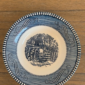May include: A blue and white ceramic saucer with a decorative border and a black and white illustration of children playing near a house.