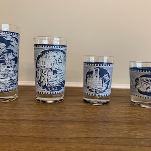 May include: Four blue and white glass tumblers with different designs. The designs are all in white and feature a scene from a historical period. The tumblers are arranged in a row from largest to smallest.