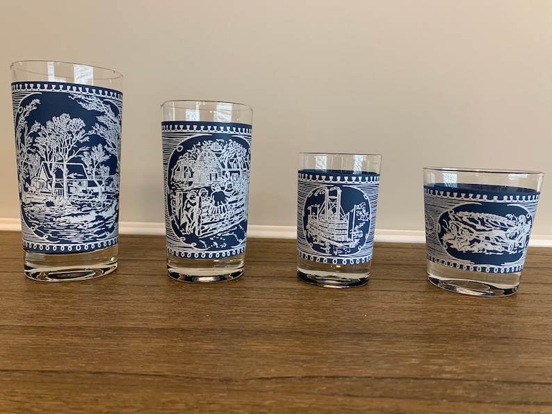 May include: Four blue and white glass tumblers with different designs. The designs are all in white and feature a scene from a historical period. The tumblers are arranged in a row from largest to smallest.