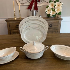 May include: A set of white porcelain dinnerware with a delicate floral pattern and gold trim. The set includes a large oval platter, three smaller plates, a gravy boat with a lid, and a serving bowl.
