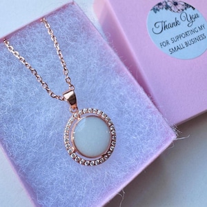 May include: Rose gold necklace with a circular pendant. The pendant has a white center stone surrounded by a ring of small, clear crystals. The necklace is displayed in a pink gift box with a sticker that reads "Thank You for supporting my small business."
