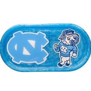 Könnte beinhalten: Eine blaue ovale Ablage mit Marmoreffekt. Sie zeigt das Logo der University of North Carolina (UNC) und ein Cartoon-Widder-Maskottchen in einem Pullover. Die Ablage ist ein dekorativer Gegenstand.