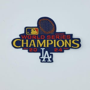 May include: Embroidered patch featuring the text "WORLD SERIES CHAMPIONS" in yellow, with the years "20" and "24" in red. The patch includes the MLB logo and the "LA" logo in white. The patch is navy blue with red and yellow accents.