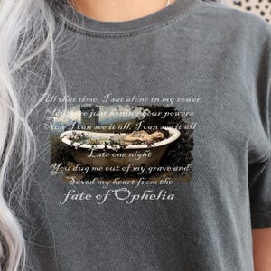May include: Dark gray t-shirt featuring a graphic of a person in a bathtub with text. The text reads "All that time, I sat alone in my tower...fate of Ophelia."
