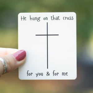 May include: White card with black text and a simple black cross. The text reads "He hung on that cross for you & for me."