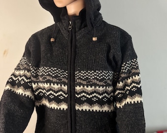 May include: A dark gray hooded zip-up sweater with a patterned design in white, black, and tan. The sweater has a hood and wooden toggles. The sweater is displayed on a mannequin.
