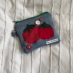 May include: Denim coin purse with a green zipper and two appliqued tomatoes. One tomato is red with white polka dots, the other is solid red. The purse has two buttons and a small tag that reads "Mai Creations."