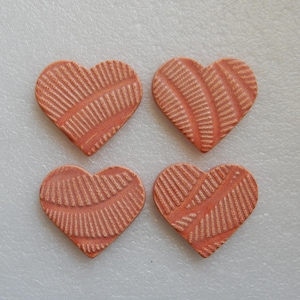 May include: Four heart-shaped decorative pieces in a warm, reddish-orange hue. Each heart features a textured, linear pattern, creating a unique design. The hearts are arranged in a square formation, perfect for crafts or embellishments.