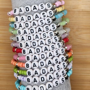 May include: A stack of 12 colorful beaded bracelets with the word "BADASS" spelled out in white beads with black lettering.