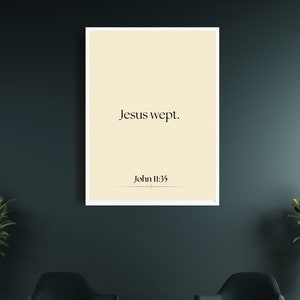 May include: A framed print with a beige background and black text that reads "Jesus wept. John 11:35". The print is hanging on a dark teal wall between two potted plants with gold pots and black stands. Two dark teal armchairs are in front of the print.