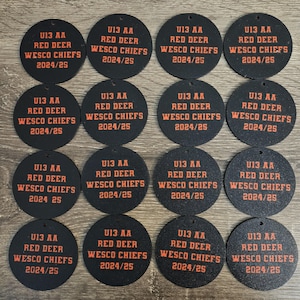 May include: Sixteen circular black ornaments featuring orange text that reads U13 AA RED DEER WESCO CHIEFS 2024/25. Each ornament has a small hole at the top for hanging. The design is consistent across all sixteen individual round pieces.