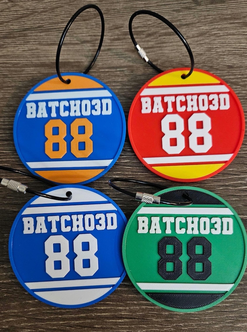 May include: Four circular luggage tags with black wire loops. Each tag features the text BATCHO3D and the number 88. The tags are blue with orange, red with yellow, blue with white, and green with black, all displaying white or black accents.