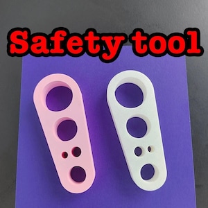 May include: Two safety tools, one pink and one white, with multiple holes of different sizes. The tools are on a purple surface.