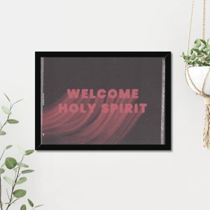 Könnte beinhalten: Ein schwarzer gerahmter Druck mit dunklem Hintergrund und rosa Schrift, die "WELCOME HOLY SPIRIT" lautet. Der Text ist über ein rosa und weißes abstraktes Design gelegt.