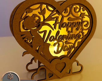 May include: A wooden heart-shaped box with a cutout design of a cupid and the words "Happy Valentine's Day". The box has a light inside and is sitting on a base with three heart cutouts.