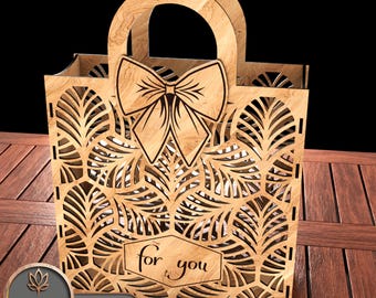 May include: A laser-cut wooden gift bag with a bow and leaf pattern. The bag has handles and the words "for you" are displayed on the front. The bag is made of light brown wood and is sitting on a wooden surface.