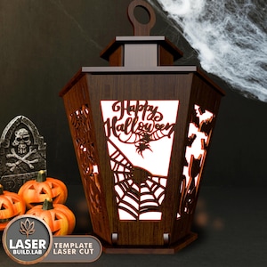 May include: A wooden lantern with a cut-out design of a spider web and the words "Happy Halloween". The lantern is lit from inside, casting a warm glow.
