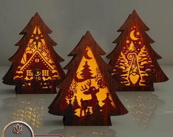 Op de afbeelding: Drie houten kerstboom-lichtdecoraties. De bomen zijn bruin en hebben verschillende uitgesneden ontwerpen. Eén boom heeft een huis, een andere een hert en de derde een kabouter.