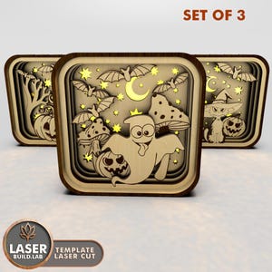 May include: Set of three laser cut wooden Halloween decorations. Each decoration features a different spooky character: a ghost, a cat wearing a witch's hat, and a pumpkin with a tree in the background. The decorations are designed to be illuminated from behind, creating a glowing effect.
