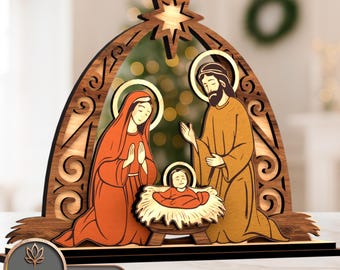 May include: A wooden nativity scene featuring Mary, Joseph, and baby Jesus, with a star above. The figures are colored in shades of orange and brown, set against a decorative wooden arch. The base has the text "LASER BUILD.LAB TEMPLATE LASER CUT".